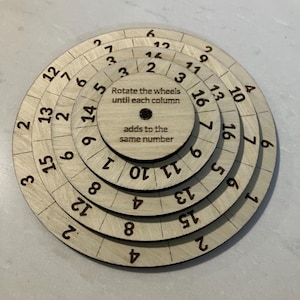 May include: A wooden puzzle with concentric rotating wheels, each marked with numbers. The center of the puzzle has text that reads "Rotate the wheels until each column adds to the same number."