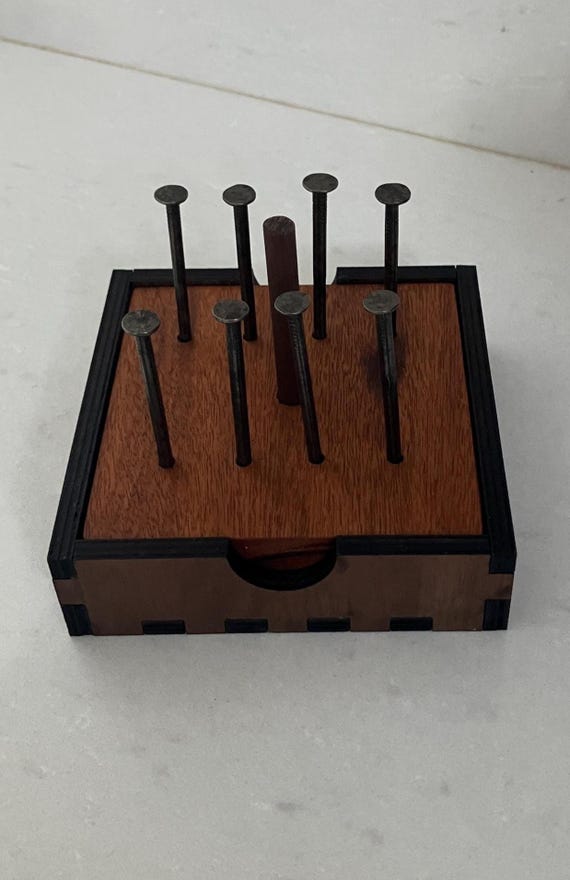 A handcrafted wooden puzzle where you balance 14 nails on a single nail head — looks physically impossible and makes everyone who sees it immediately need to try it.