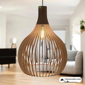 May include: A wooden pendant light fitting with a bulb visible inside. The light has a brown top and a light brown, cage-like shade. The fitting is suspended from a black cord. The website "harzworks.com" is visible in the bottom right corner.