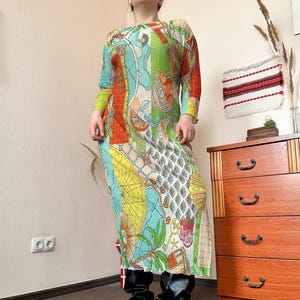 Puede incluir: Un vestido largo y colorido con un diseño de patchwork. El vestido presenta una variedad de patrones y colores, incluyendo rojo, verde, amarillo y azul. Tiene mangas largas y un cuello redondo. El vestido se lleva con botas negras.