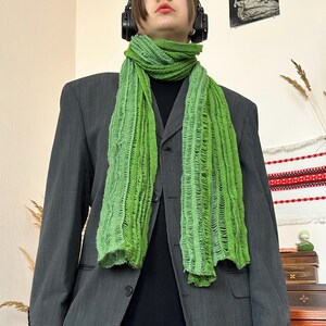 May include: A bright green scarf with a textured, open weave design. The scarf is draped over a dark gray blazer. The scarf's color transitions from a darker green at the top to a lighter, brighter green towards the bottom. The scarf is a fashion accessory.
