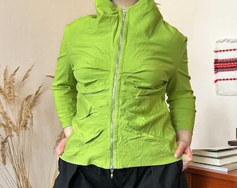 May include: A bright green jacket with a high collar and a full-length silver zipper. The long-sleeved jacket has a ruched design and is paired with black pants. The jacket is a vibrant, eye-catching piece.