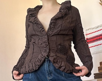 May include: A brown, textured jacket with ruffled trim and floral embellishments. The jacket has long sleeves and a button closure. The style is vintage and unique.