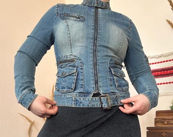May include: A light blue denim jacket with a stand-up collar, zipper closure, and multiple pockets. The jacket features a belt at the waist and a fitted silhouette. The sleeves are long and the denim has a faded wash.