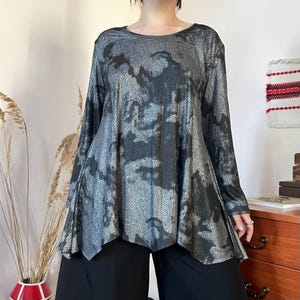 Op de afbeelding: Een tuniek met lange mouwen en een gemêleerd patroon in metallic zilver en zwart. Het kledingstuk heeft een ronde halslijn en een uitlopende, asymmetrische zoom die zorgt voor een losvallend, vloeiend silhouet met een glinsterende textuur.