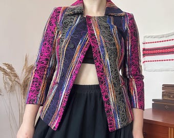 May include: A structured blazer featuring a dark base with vertical stripes and intricate, overlapping neon pink and grey circular line patterns. The jacket has a notched collar, three-quarter length sleeves, and two black buttons on the front closure.