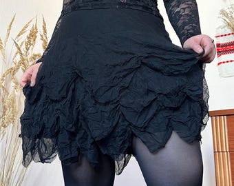 May include: A black skirt with a layered, ruffled design. The skirt is paired with a black lace top with long sleeves. The image shows the skirt being held up, showcasing the texture and style of the garment.