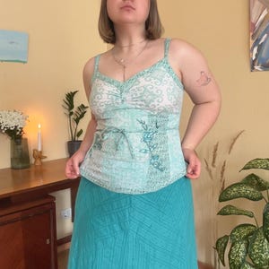 May include: A light blue and white patterned camisole top with spaghetti straps and a matching light blue skirt. The top has a tie at the waist and floral embroidery. The skirt is a solid light blue color.
