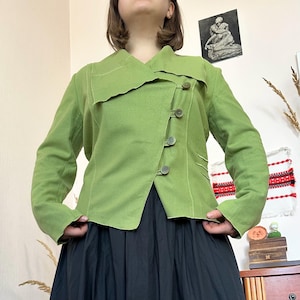 以下が含まれることがあります： ユニークな非対称デザインのライトグリーンのジャケット。 ジャケットは大きな襟、3つのボタン留め、長袖が特徴です。 ジャケットは黒いスカートと組み合わせています。
