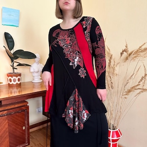 May include: Black and red long-sleeved tunic with floral and paisley patterns. The tunic features a red vertical stripe and a layered asymmetrical design. The bottom portion is a solid black skirt.