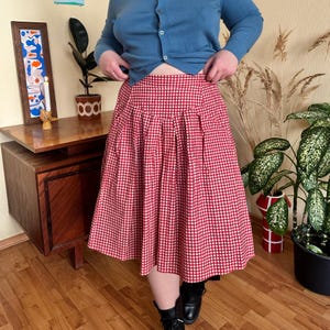 Puede incluir: Una falda a cuadros rojos y blancos con pliegues. La falda a la rodilla se combina con una rebeca azul y botas negras. El patrón de la falda es un diseño de cuadros clásico, adecuado para ropa informal.