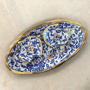 Op de afbeelding: Een keramische serveerset met een blauw-wit bloemmotief en gouden rand. De set bevat een ovale schaal en twee kleinere schaaltjes, elk met een gouden Davidster. Er is Hebreeuwse tekst zichtbaar.