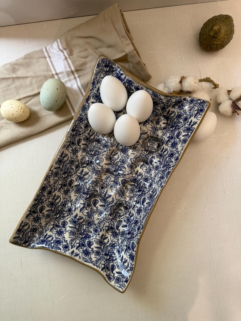 A rectangular ceramic egg holder with a blue floral pattern and a gold rim