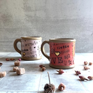 Pair of handcrafted ceramic mugs featuring love words in various languages, 24k gold hearts on body and handle, surrounded by dried roses and sugar, ideal for galentines or valentines gifting