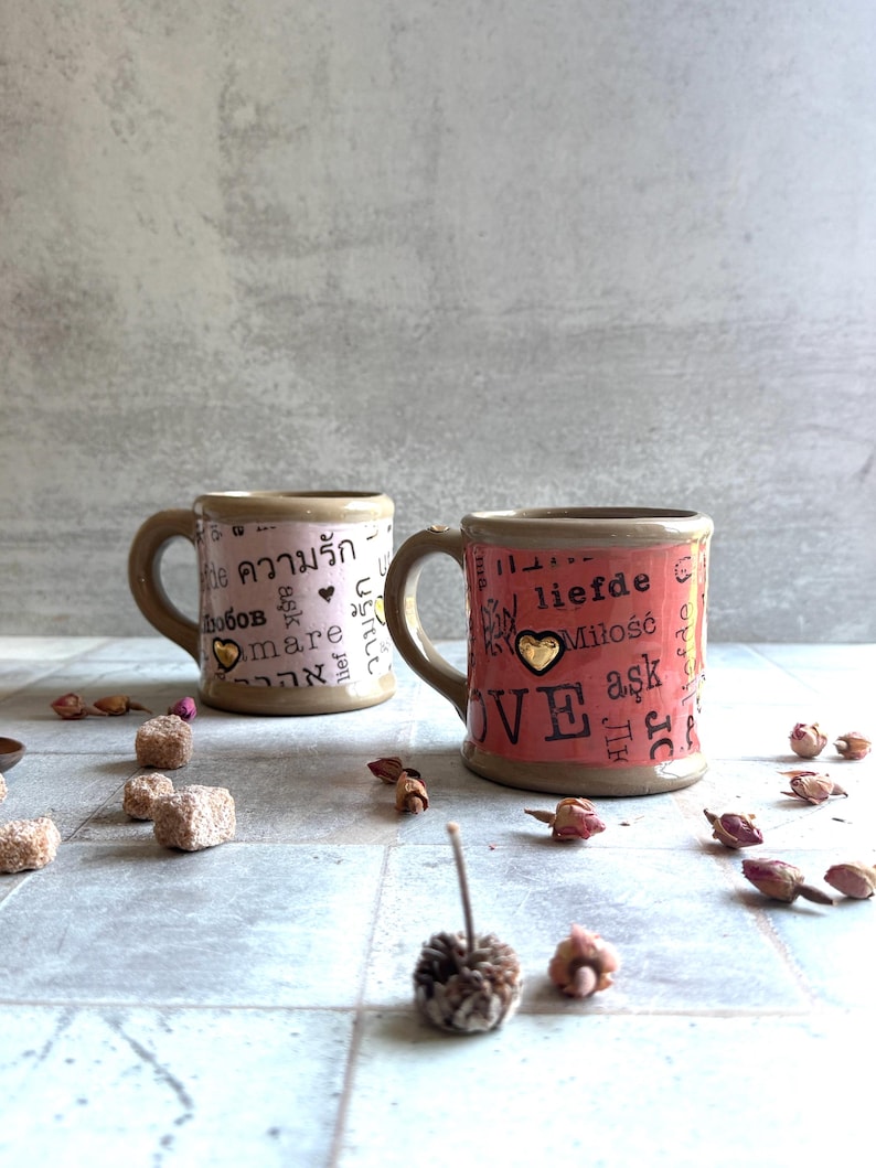 Pair of handcrafted ceramic mugs featuring love words in various languages, 24k gold hearts on body and handle, surrounded by dried roses and sugar, ideal for galentines or valentines gifting