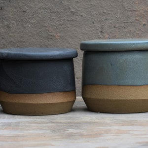 Peut inclure: Quatre pots en c&eacute;ramique avec couvercles. Chaque pot pr&eacute;sente une base marron clair et des sections sup&eacute;rieures de couleurs violet, noir, vert d'eau et blanc. Les couvercles reprennent la couleur sup&eacute;rieure de chaque pot.