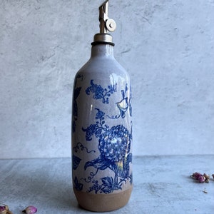 A white ceramic oil and vinegar bottle with a blue floral design and a silver pour spout.