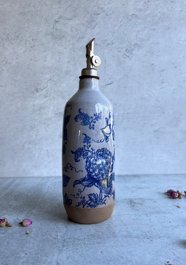 A white ceramic oil and vinegar bottle with a blue floral design and a silver pour spout.