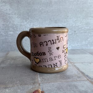 Handmade pottery coffee mug in violet tone with words of affection in various languages and 24k gold accent, plus dried rose props, ideal for galentines or relationship tokens