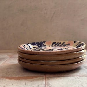 May include: A stack of four small, round ceramic plates. The plates have a brown exterior and a white interior with a blue and pink floral pattern. The plates are stacked on top of each other.