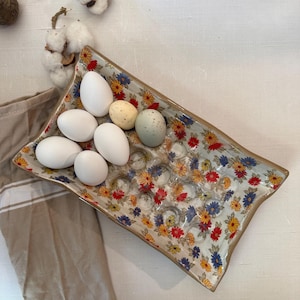 May include: A floral patterned ceramic egg holder with six white eggs and two speckled eggs. The holder is a rectangular shape with a raised edge.