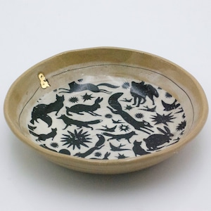 Puede incluir: Un cuenco de cer&aacute;mica beige con un dise&ntilde;o en blanco y negro de animales y estrellas. El cuenco tiene un acento dorado en el borde.