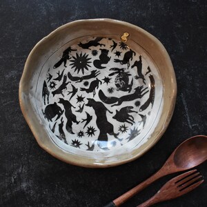 Puede incluir: Un taz&oacute;n de cer&aacute;mica blanca con un dise&ntilde;o en blanco y negro de animales y estrellas. El taz&oacute;n tiene un borde ligeramente redondeado y un esmalte beige.