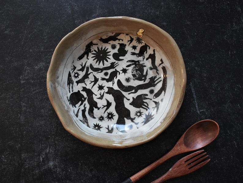 Puede incluir: Un taz&oacute;n de cer&aacute;mica blanca con un dise&ntilde;o en blanco y negro de animales y estrellas. El taz&oacute;n tiene un borde ligeramente redondeado y un esmalte beige.