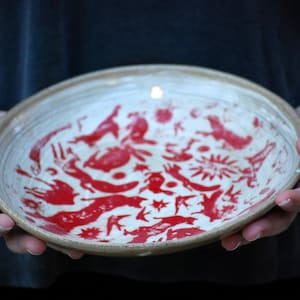 May include: A white ceramic bowl with a red design of stylized animals and geometric shapes.