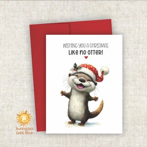 May include: A Christmas card featuring a smiling otter wearing a Santa hat with holly. The card reads "Wishing you a Christmas Like no otter!" with a red envelope behind it. The Sunnyside Card Shop logo is in the lower left corner.