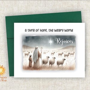 May include: A Christmas card with a watercolor illustration of a shepherd and child with sheep under a starry sky. The text reads "a thrill of hope, the weary world rejoices." The card is paired with a green envelope.
