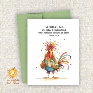 May include: Greeting card with a watercolor illustration of a colorful rooster holding a coffee cup. The card has the text "THE OLDER I GET, the more I understand why roosters scream to start their day." A green envelope is behind the card.
