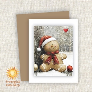 May include: A Christmas card featuring a gingerbread man wearing a Santa hat and scarf, leaning against a snowy tree. The card has a brown envelope and the text "Sunnyside Card Shop". Ornaments and a red heart are also visible.