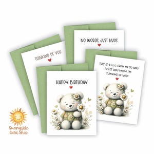 May include: Greeting cards with a cute teddy bear design. The cards have messages like "Happy Birthday" and "Thinking of You." Each card features a white teddy bear holding daisies, with a green plaid shirt and a daisy crown. The cards are paired with green envelopes.
