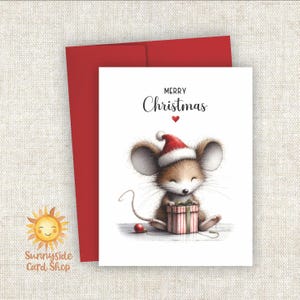May include: A Christmas card featuring a cute mouse wearing a Santa hat and holding a gift. The card has the words "Merry Christmas" and a red heart. A red envelope is behind the card.