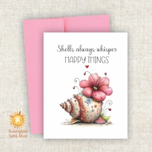 May include: A greeting card with a pink envelope. The card features a watercolor illustration of a seashell with a pink flower and the text "Shells always whisper HAPPY THINGS."