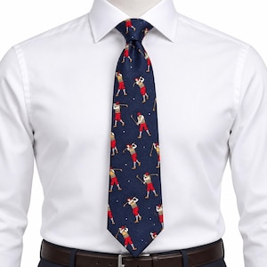May include: A dark navy blue necktie featuring a repeating pattern of golfers in red trousers and yellow sweaters swinging golf clubs. The tie is worn over a crisp white button-down shirt with a dark brown leather belt visible at the waistline.