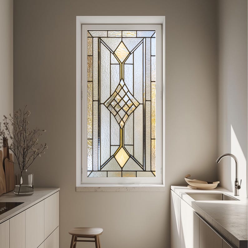 May include: A rectangular stained glass window with a white frame. The design features geometric shapes in shades of yellow, gold, and clear glass, with black lines defining the patterns. The window is set in a kitchen setting.