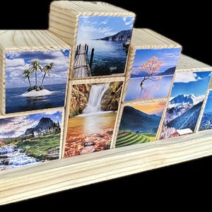 Peut inclure: Un ensemble de neuf blocs en bois avec des images de paysages différentes imprimées sur chaque face. Les blocs sont disposés en forme de pyramide sur une base en bois. Les images comprennent une cascade, une chaîne de montagnes, une île tropicale, un lac avec un arbre, un horizon de ville et un champ de rizières.