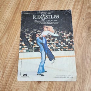 May include: Sheet music cover for "Theme From Ice Castles (Through The Eyes Of Love)". The cover features a couple ice skating. The man is holding the woman in the air. The background shows a stadium.