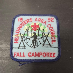 May include: A square patch with a light blue background and a dark blue border. The patch features the text "HEADWATERS AREA COUNCIL 92" and "FALL CAMPOREE" in red. A silhouette of a person on a rope bridge is in the center.