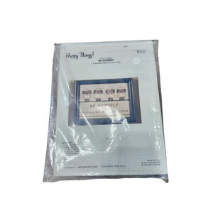 May include: A cross-stitch kit by Happy Things! featuring a framed design with four sheep and the text "BE YOURSELF." The kit is packaged in a clear plastic bag. The design measures 5" x 7".