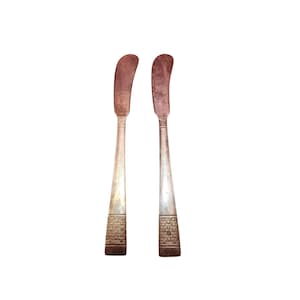 May include: Two antique butter knives with curved blades and silver handles. The handles have a textured brick-like pattern near the base. The blades have a reddish-brown patina, and the handles show signs of wear.
