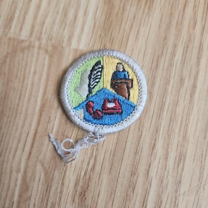May include: Embroidered patch with a circular design. The patch features a blue, yellow, and green color scheme with images of a building, a person at a podium, and a red telephone. The patch has a white border and loose threads.