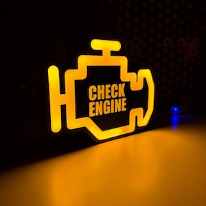 Pode incluir: Um sinal amarelo iluminado em forma de luz de advertência do motor do carro com o texto "CHECK ENGINE" dentro.