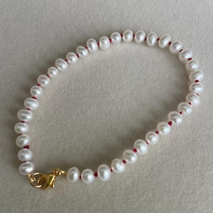 May include: A white pearl bracelet with a red string and a gold clasp.