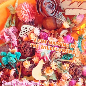 May include: A collection of dried flowers, pinecones, and wooden cutouts including a fox, mushrooms, and feathers. The text A FOX NAPPING IN THE WILDFLOWERS is centered, and the text Pretty PrairieSoul is at the bottom in a pink script font.