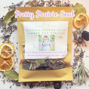 Könnte beinhalten: Ein brauner Papierbeutel mit einem weißen Etikett, auf dem "Pretty Prairie Soul" und "Nature Flower Soup Simmer Pot Version" steht. Das Etikett zeigt auch eine Cartoon-Illustration eines weißen Kaninchens mit einer Blumenkrone. Der Beutel ist von getrockneter Lavendel, Zitronenscheiben und Lorbeerblättern umgeben.