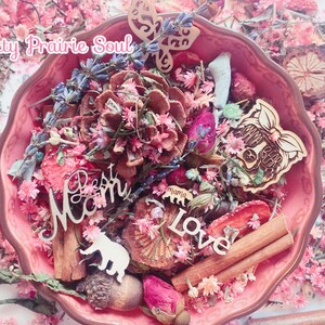 May include: A pink bowl filled with dried flowers, cinnamon sticks, pinecones, and wooden ornaments. The ornaments include a butterfly, a bear with the text "Mama Bear", and the words "Best Mom" and "Love".