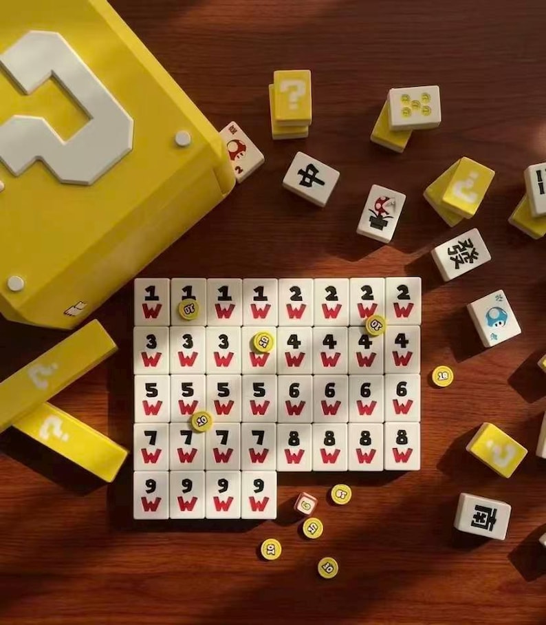 Puede incluir: Una caja amarilla con un signo de interrogaci&oacute;n blanco y una colecci&oacute;n de fichas de juego. Las fichas son blancas con n&uacute;meros negros, caracteres chinos y s&iacute;mbolos 'W' rojos. Algunas fichas son amarillas con signos de interrogaci&oacute;n.